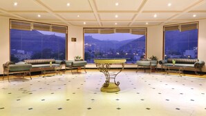 Eine geräumige Lobby mit einem zentralen, verzierten Tisch, großen Fenstern mit Blick auf die Berge und gemütlichen Sitzbereichen.
