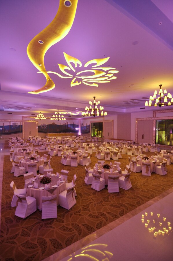 A large banquet hall with round tables and chairs, chandeliers, and a decorative ceiling design.