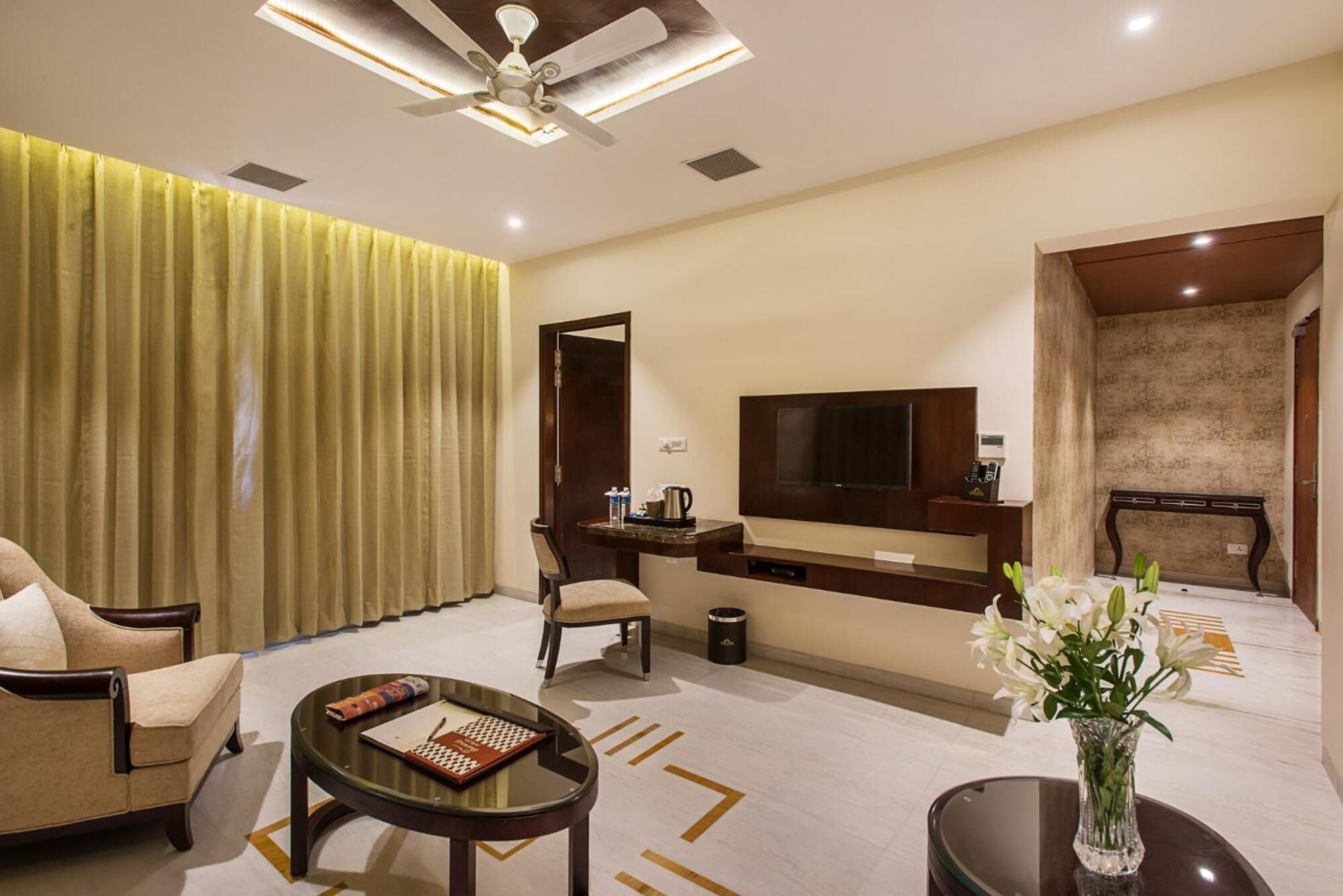 A hotel room with a sofa, a coffee table, a TV, a desk, and a vase with flowers.