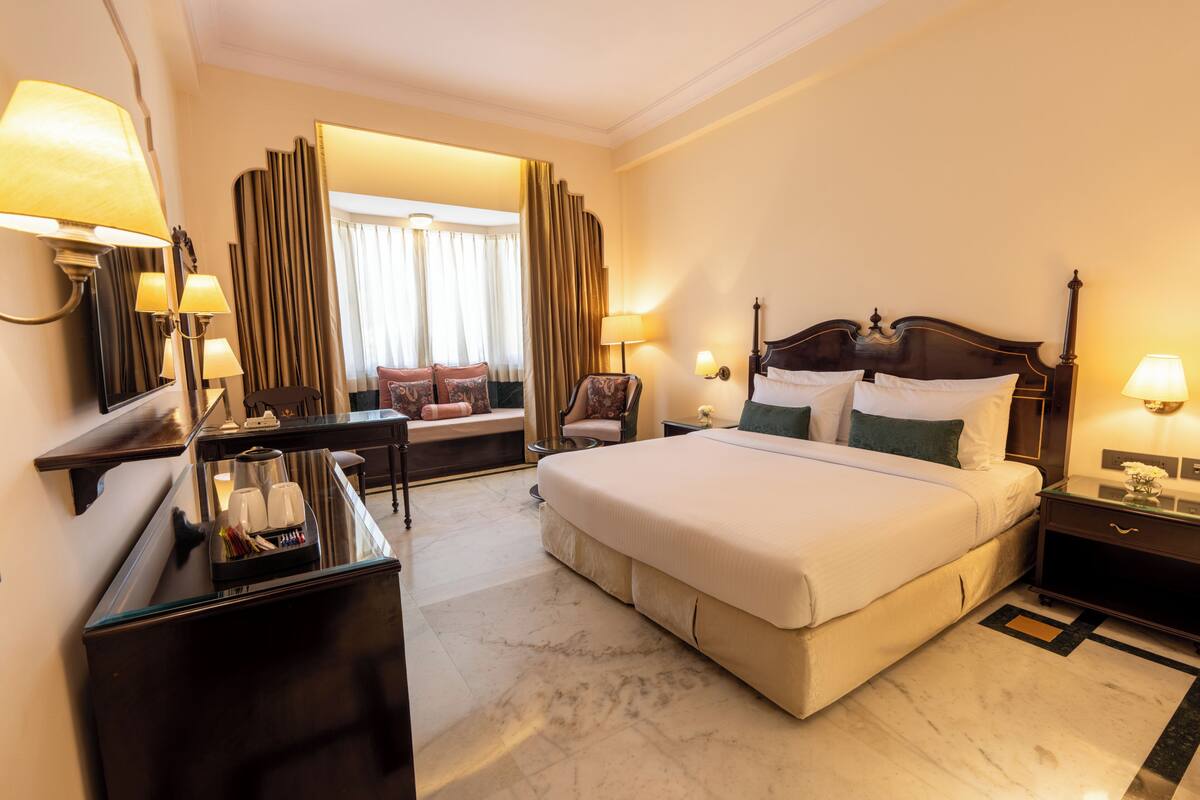 A hotel room with a large bed, bedside tables, a desk, and a seating area with a view of the outdoors.