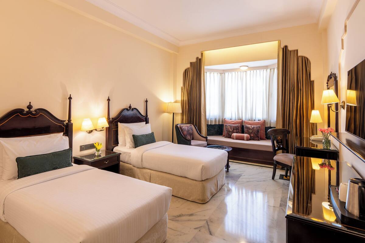A hotel room with two beds, a sofa, a chair, a mirror, and a lamp.