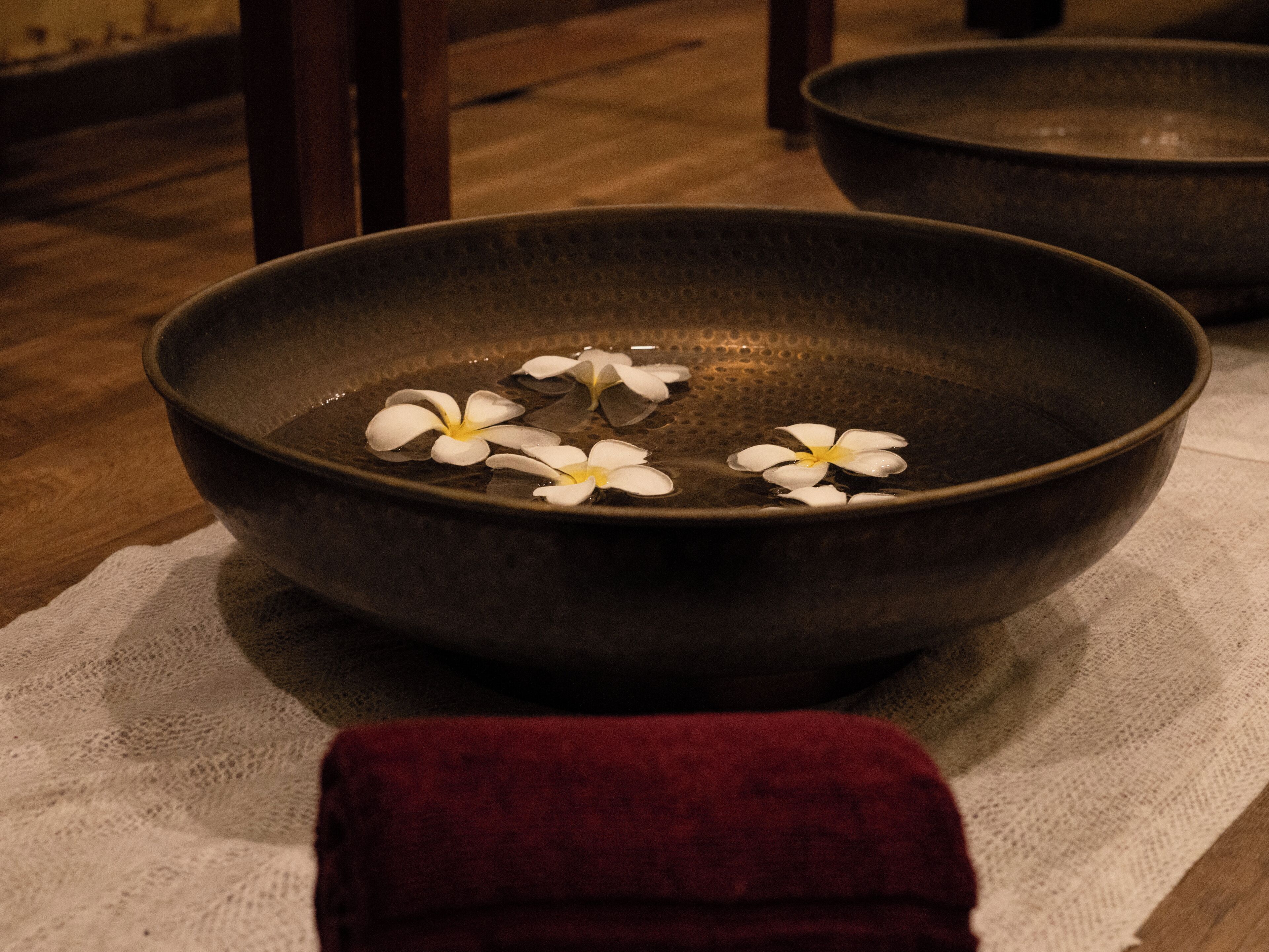 A dark bowl with water and white flowers on a white cloth.