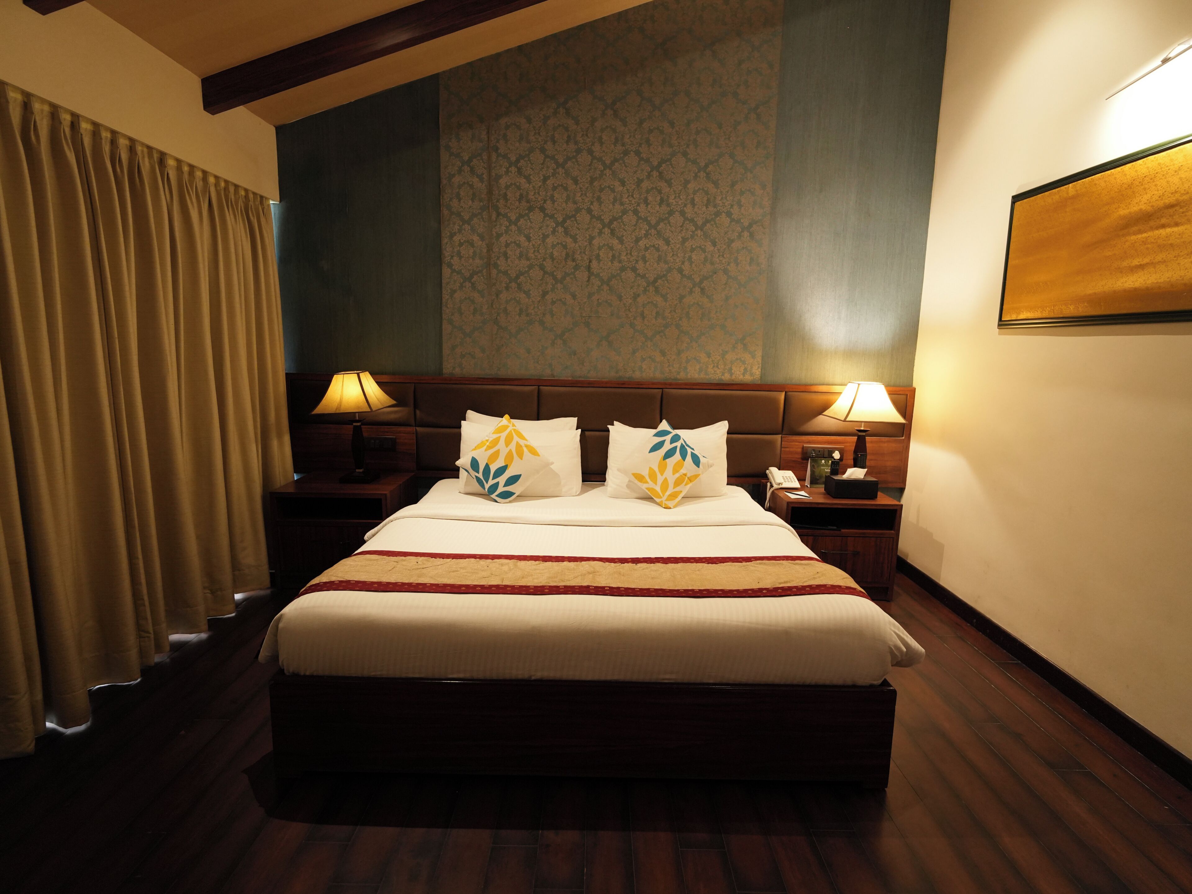 Quarto de hotel com uma cama grande, duas mesas de cabeceira com luminárias, um telefone e uma televisão fixada na parede.