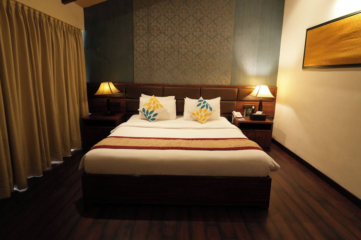 Habitación de hotel con una cama grande, dos mesitas de noche con lámparas, un teléfono y un televisor montado en la pared.