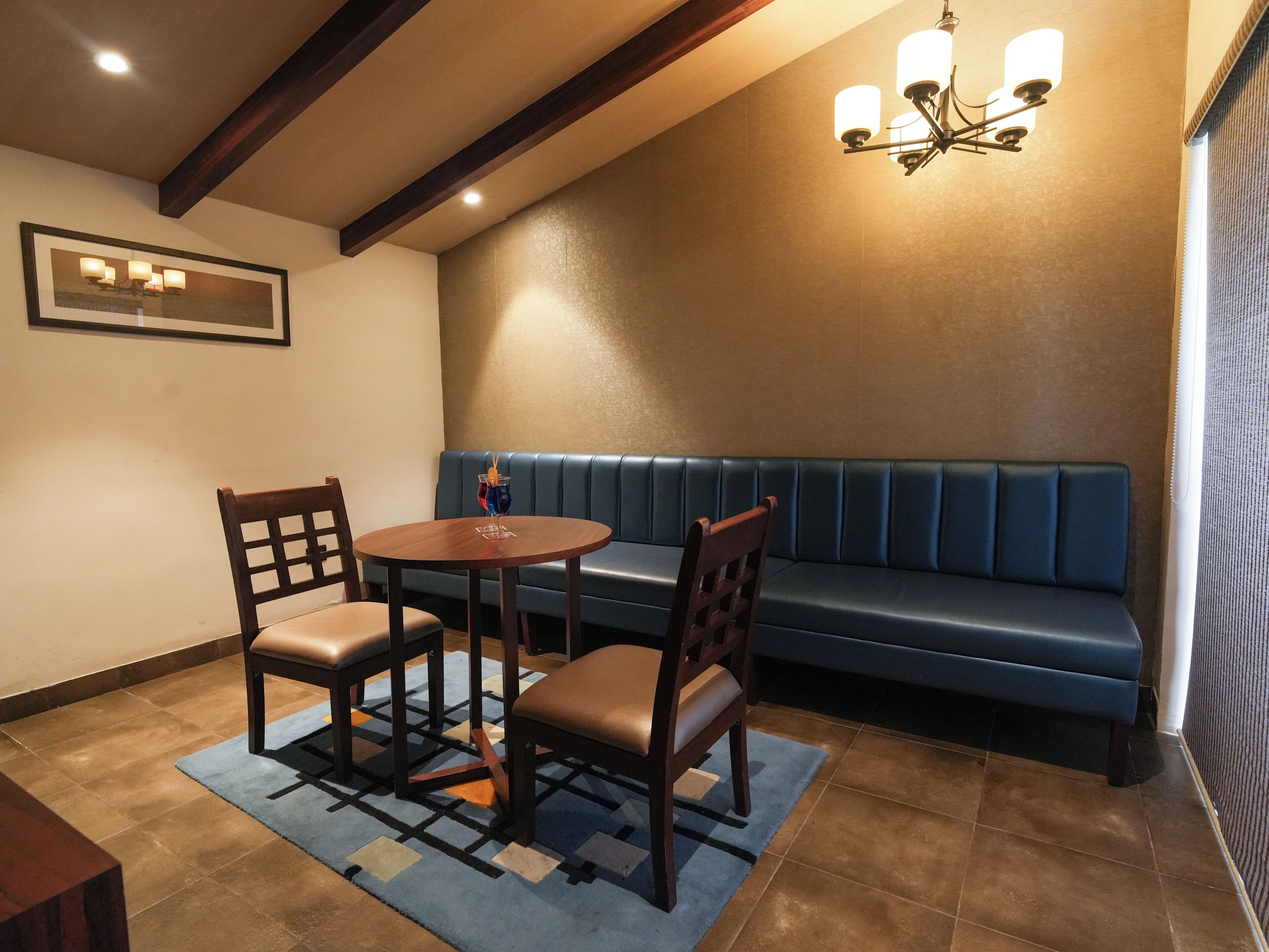 A room with a blue cushioned bench, a round wooden table with two chairs, and a chandelier.