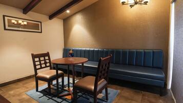A room with a blue cushioned bench, a round wooden table with two chairs, and a chandelier.