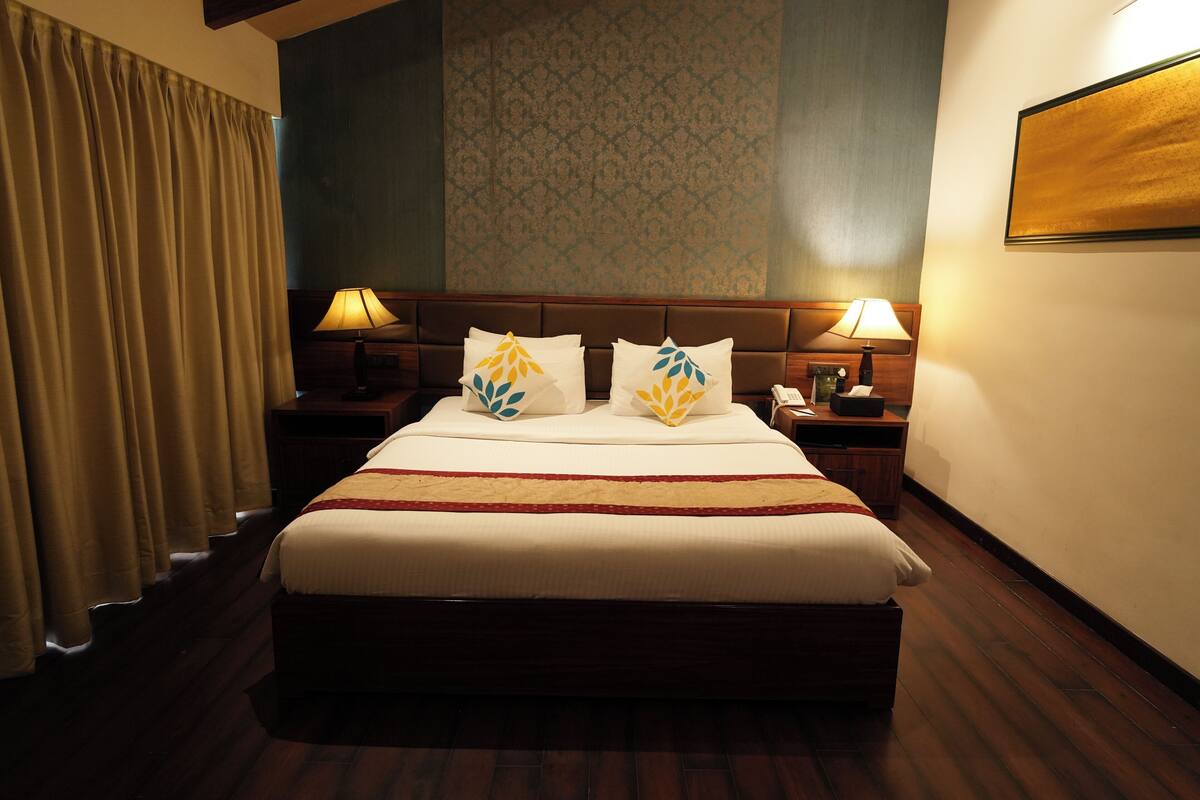 Habitación de hotel con una cama grande, dos mesitas de noche con lámparas, un teléfono y un televisor montado en la pared.