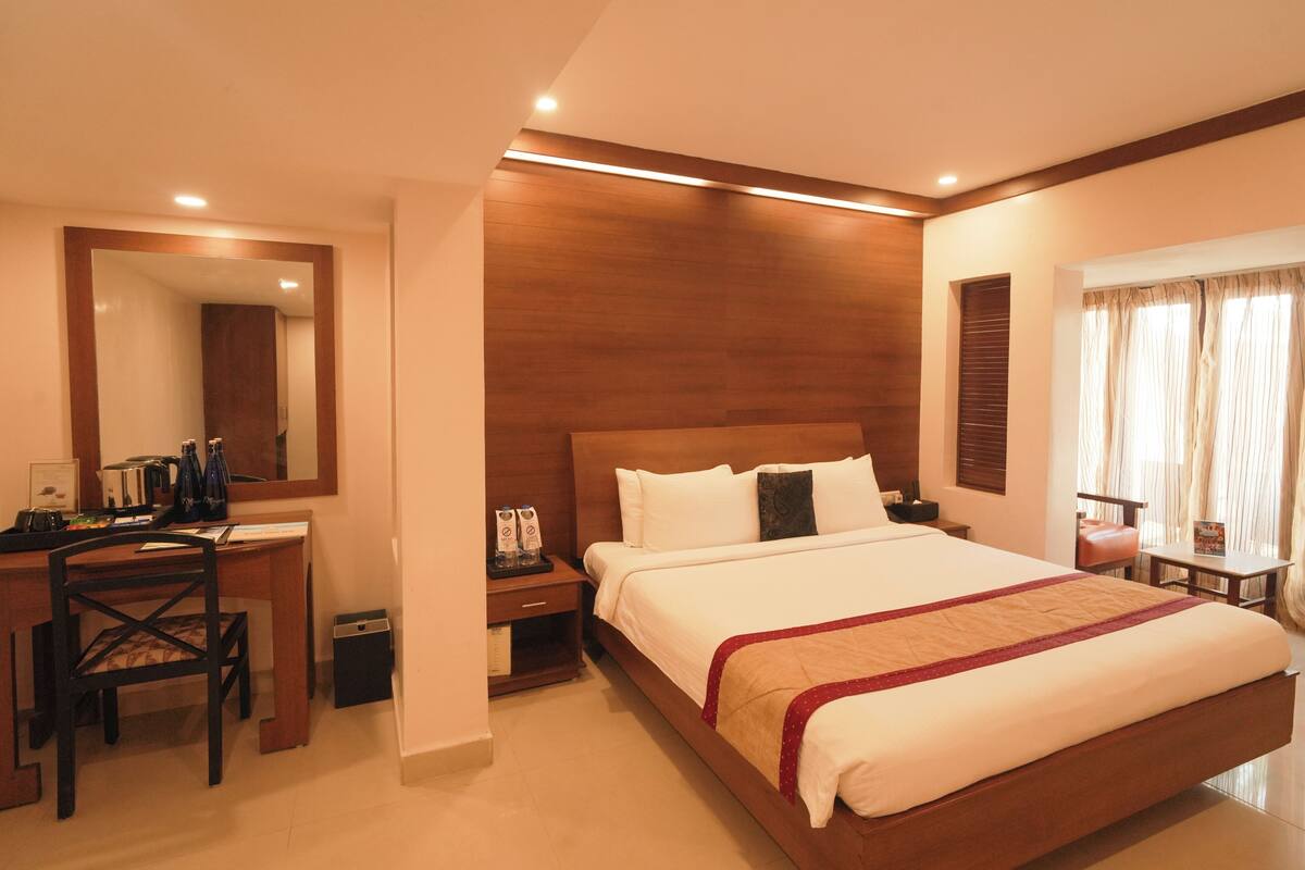 Una habitación de hotel con una cama grande, un escritorio con silla, una mesita y un espejo.