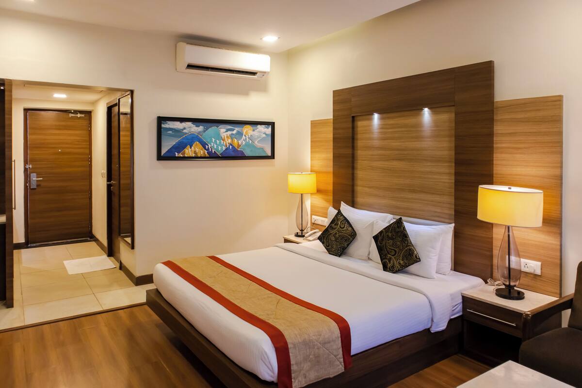 Habitación de hotel con una cama grande, dos lámparas de noche, un cabecero de madera, un cuadro en la pared y un equipo de aire acondicionado.
