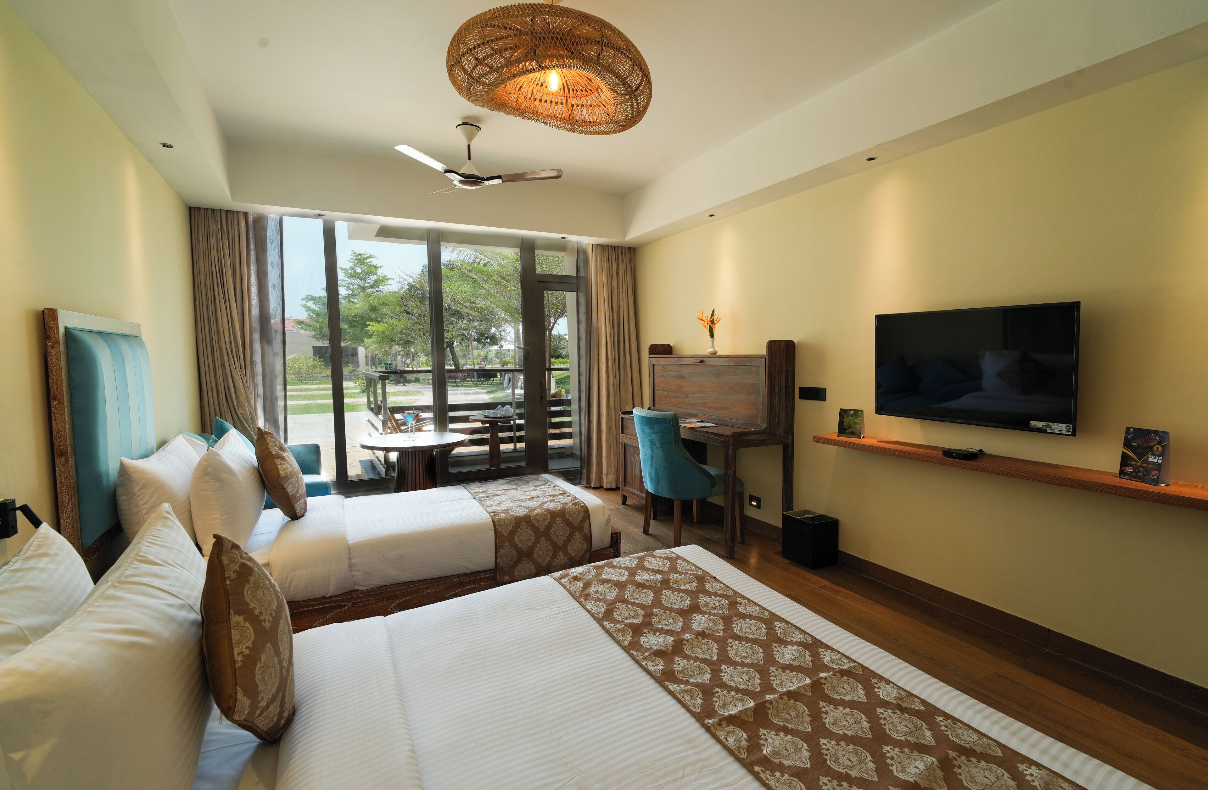 A hotel room with two beds, a TV, a desk, and a view of the outdoors.