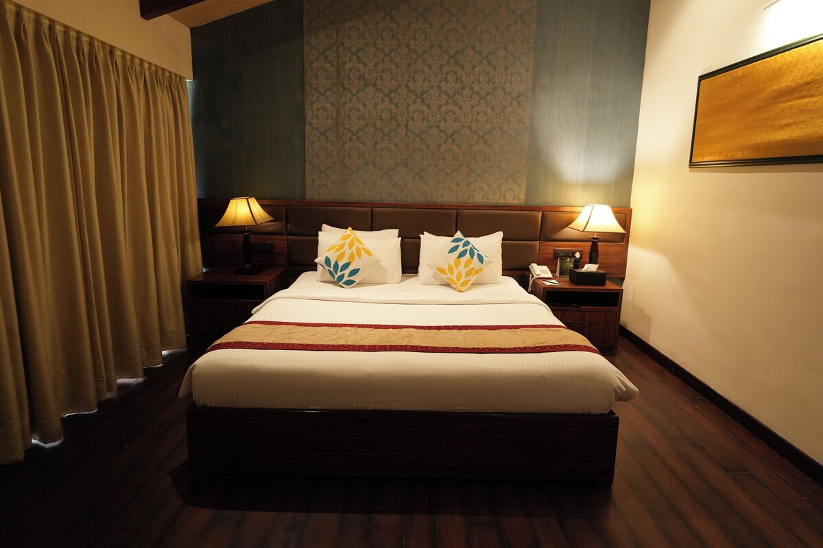 A hotel room with a large bed, two bedside tables with lamps, a telephone, and a wall-mounted TV.