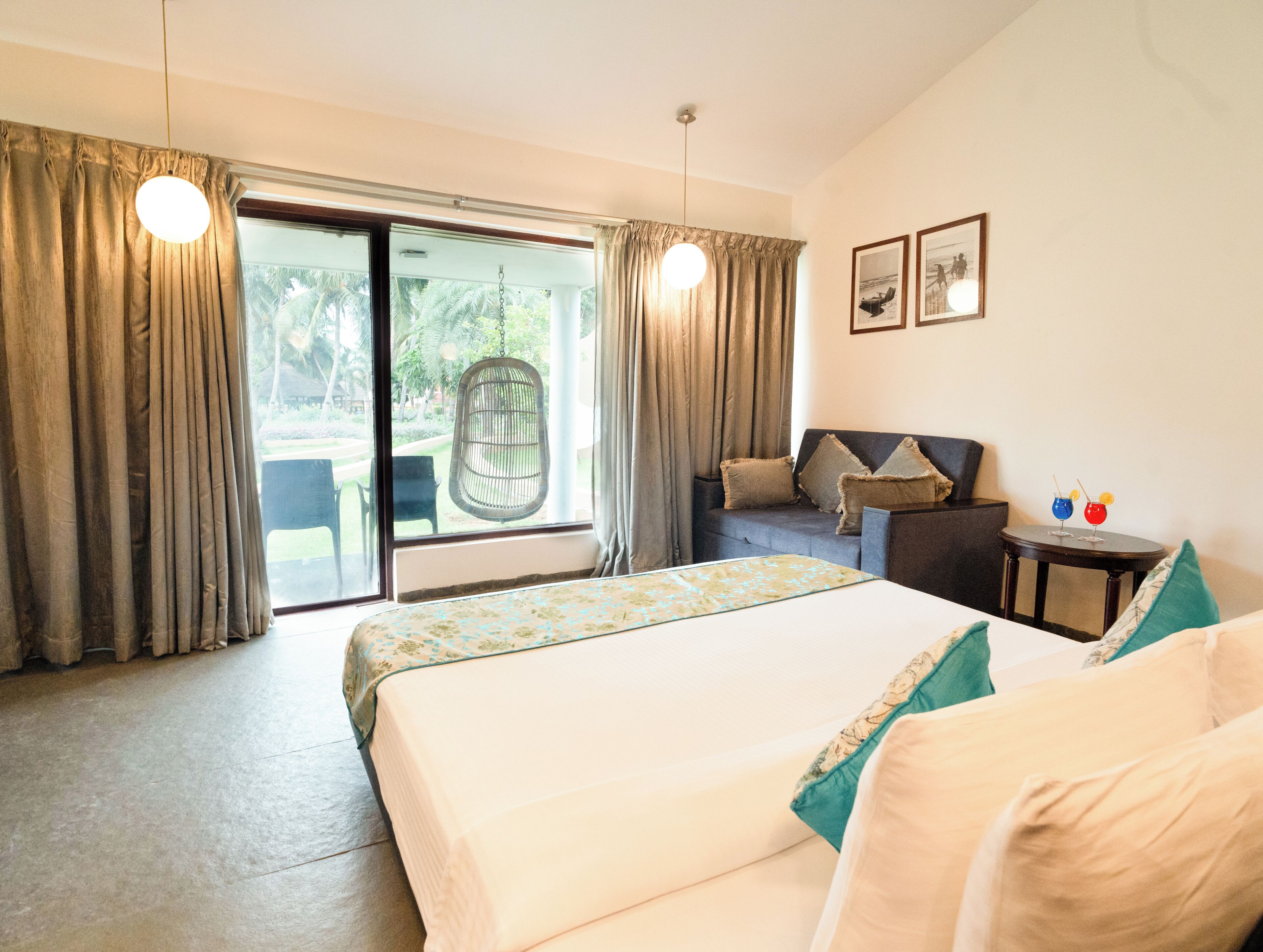Quarto de hotel com cama, sofá, uma mesinha com bebidas e vista através de uma porta de correr.