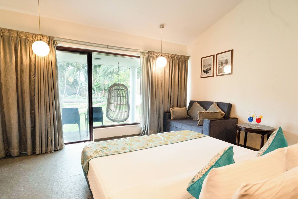 Una habitación de hotel con cama, sofá, una mesita con bebidas y una silla al lado de la ventana.
