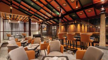 Un restaurant avec de hauts plafonds, des poutres décorées de motifs orange et verts, et un coin bar équipé de tabourets.