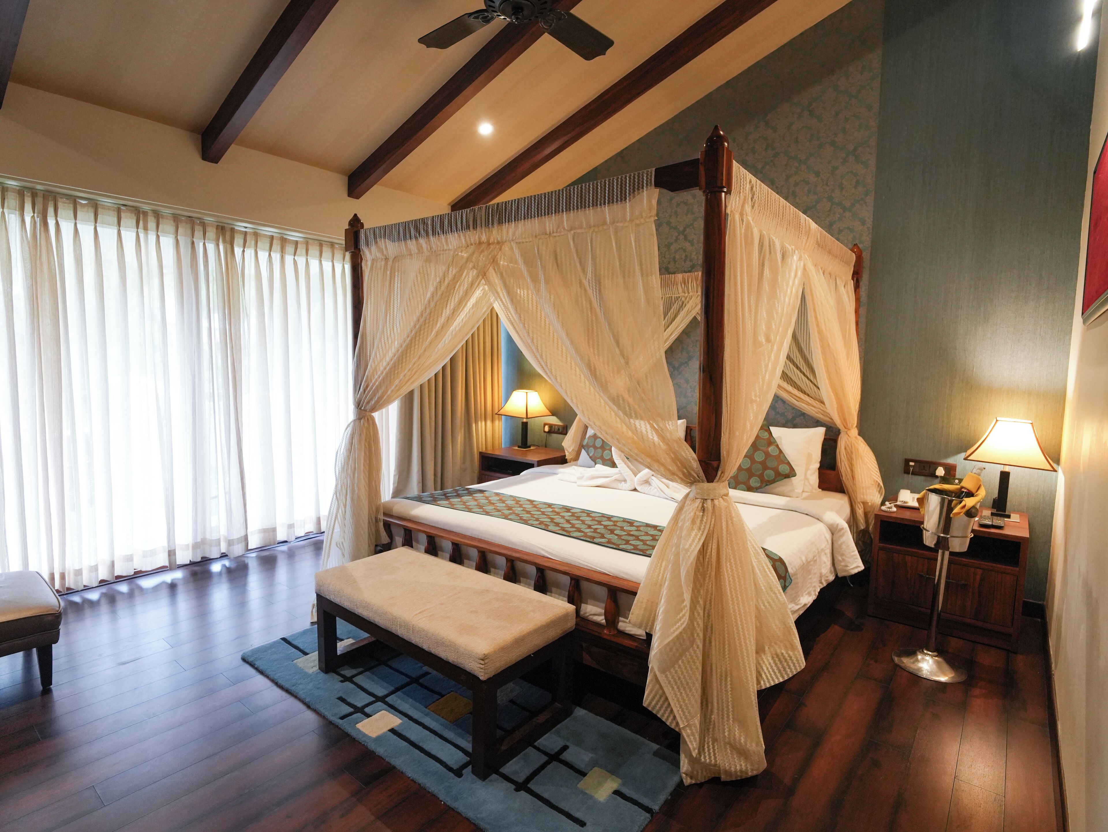A four-poster canopy bed with a bench, bedside tables, and a nightstand with a lamp.