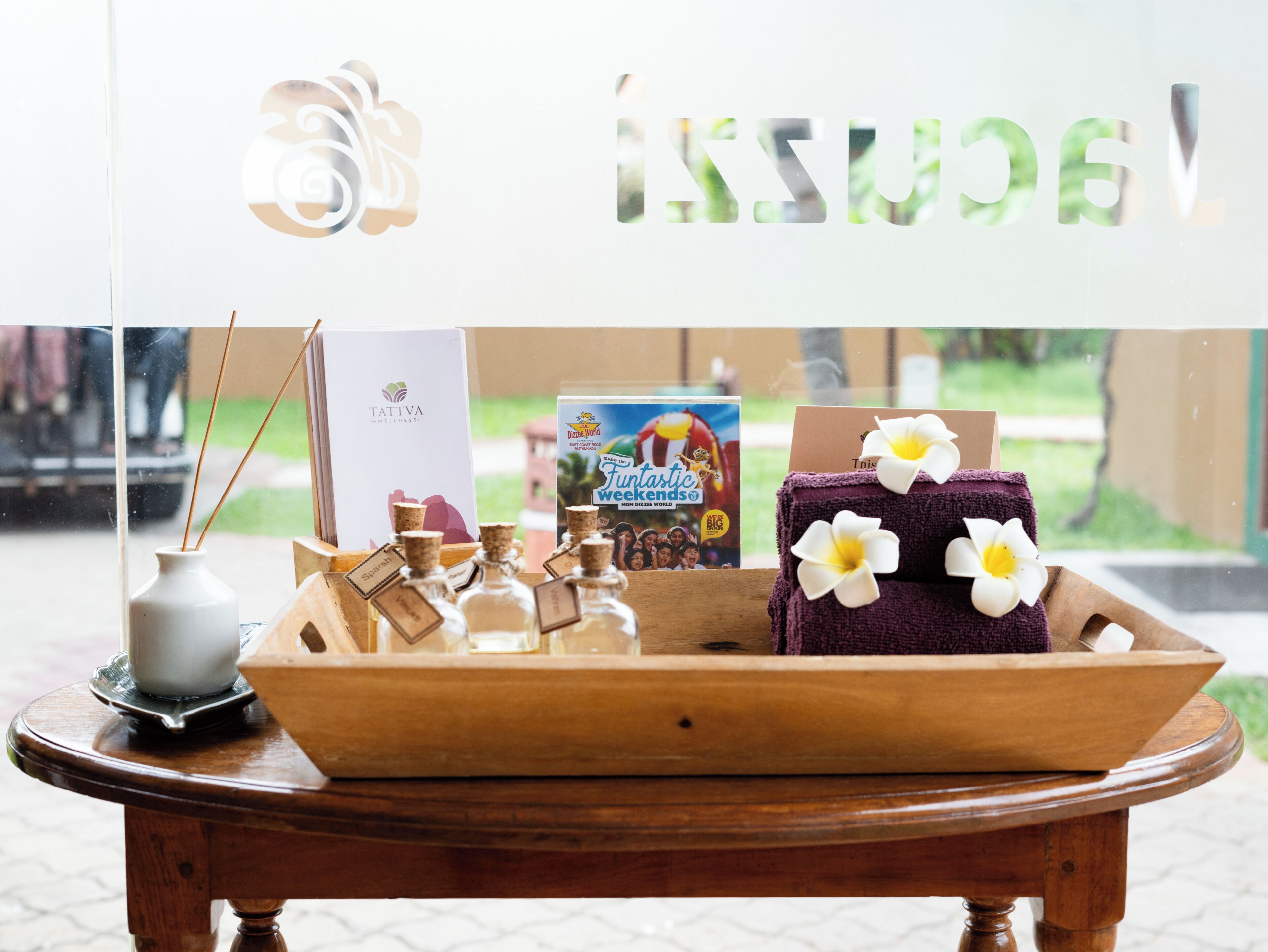 A wooden tray with a towel and a bottle of essential oils on a table, with a window displaying a sign and a book.