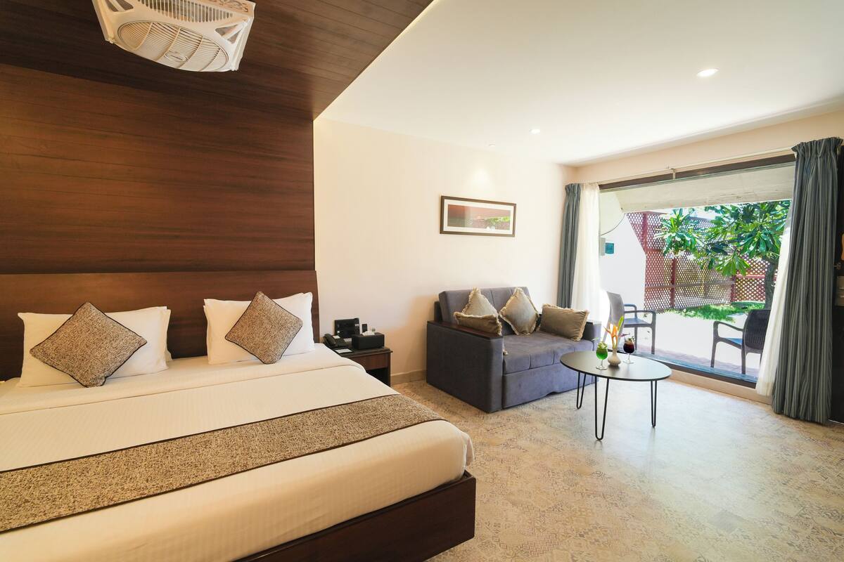 Habitación de hotel con una cama grande, un sofá, una mesita y vistas al exterior.