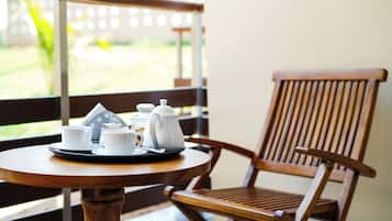 A wooden table with a tray of white cups and a teapot, positioned near a window with a view of greenery.