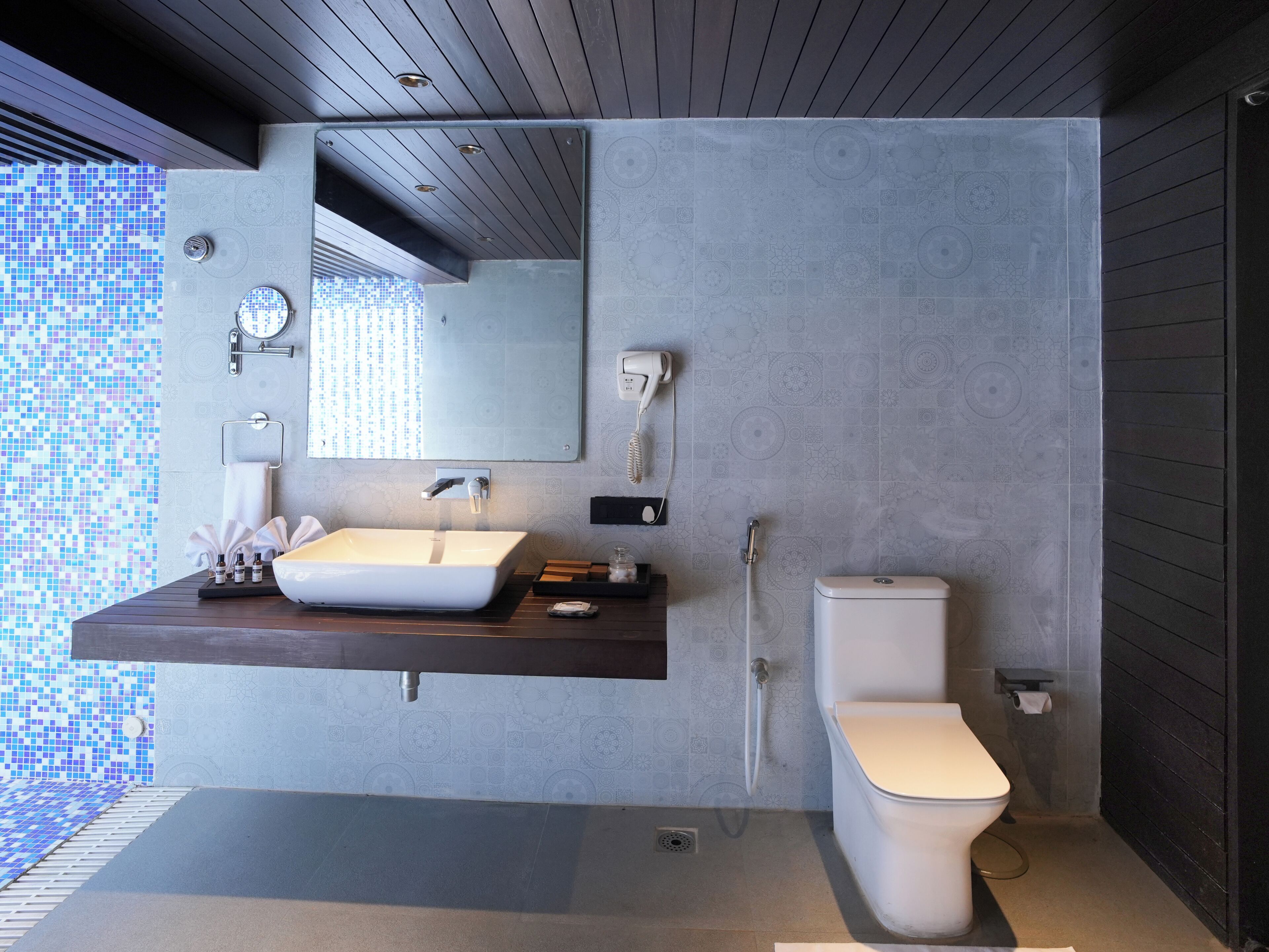 A modern bathroom with a large mirror, a white sink, a toilet, and a shower.