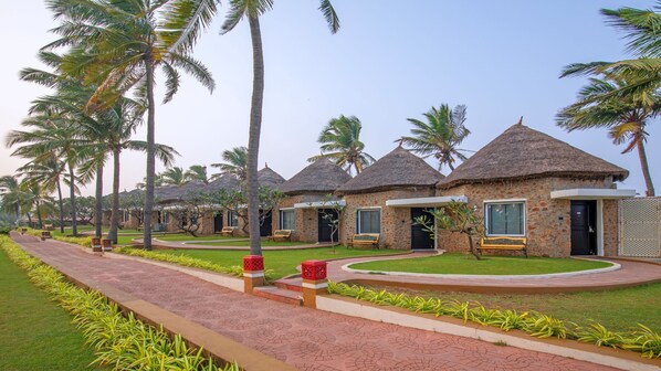 A row of thatched-roof cottages with a paved walkway and palm trees. - MGM Beach Resorts (Tirupporur)