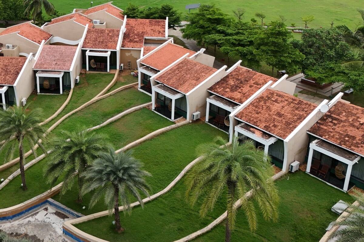 Un conjunto de villas modernas con tejados de tejas rojas, rodeadas de céspedes cuidados y palmeras.