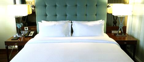 Habitación de hotel con una cama grande, dos mesitas de noche, un cabecero tapizado en verde y dos lámparas de noche.