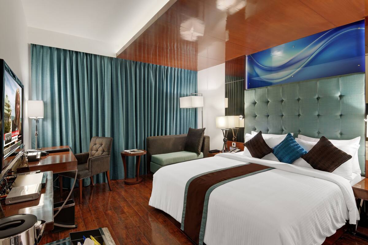 A hotel room with a large bed, a desk with a computer, a chair, and a TV.