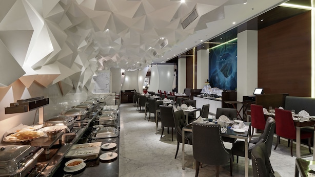 Un comedor moderno con diseño geométrico en el techo, suelo de mármol y mobiliario contemporáneo.