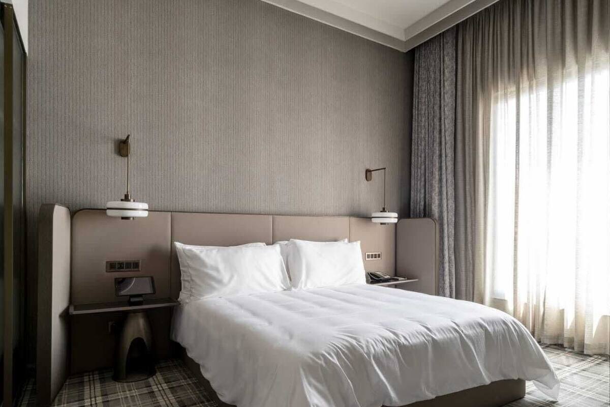 A hotel room with a large bed, two bedside tables, a headboard, and a view of the city through curtains.