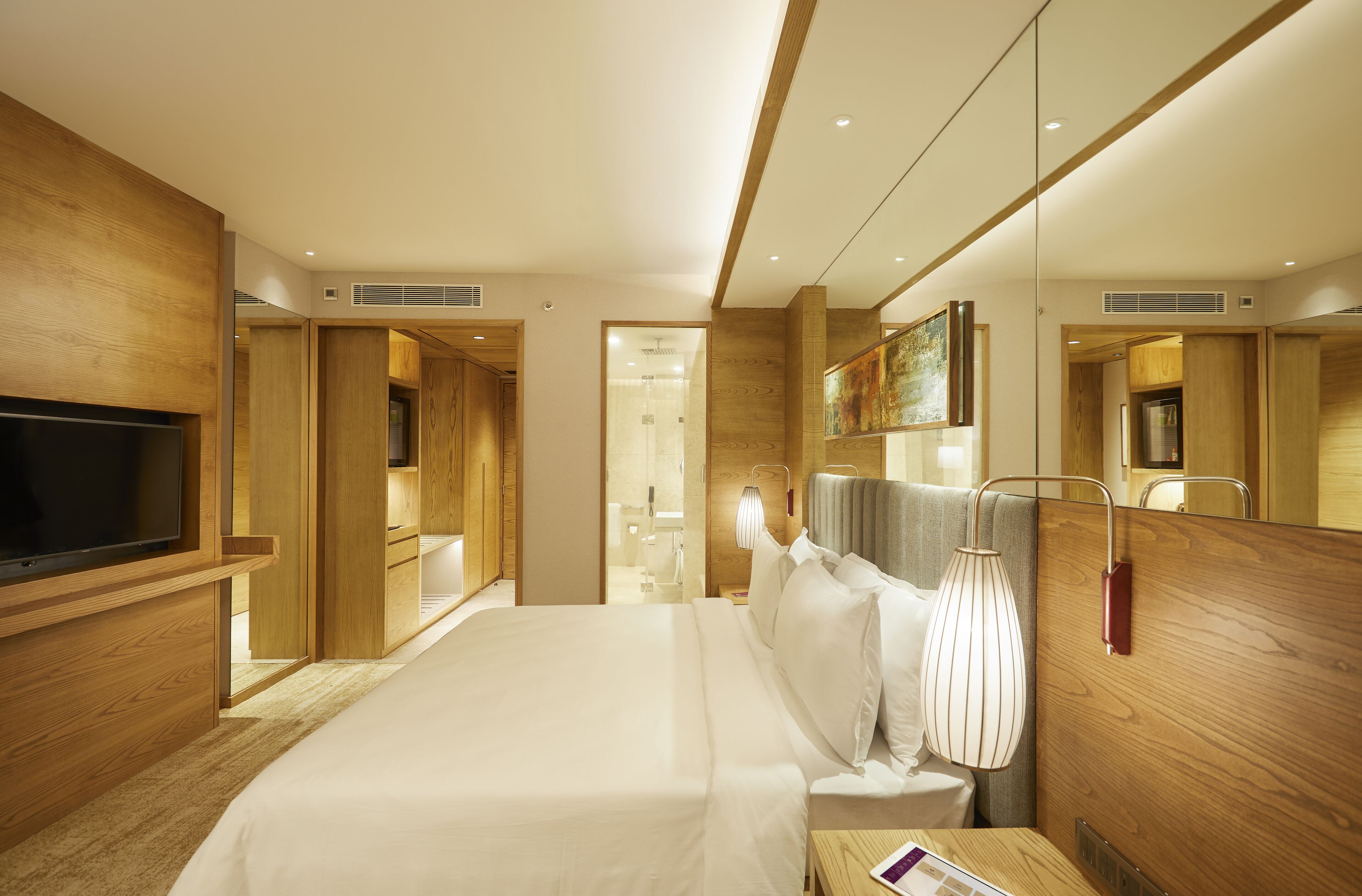 A modern hotel room with a large bed, wooden paneling, a flat-screen TV, and a bathroom visible through an open door.