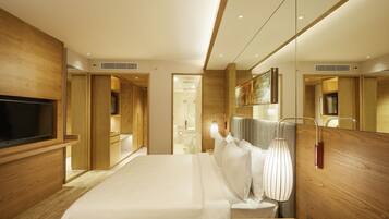 A modern hotel room with a large bed, wooden paneling, a flat-screen TV, and a bathroom visible through an open door.