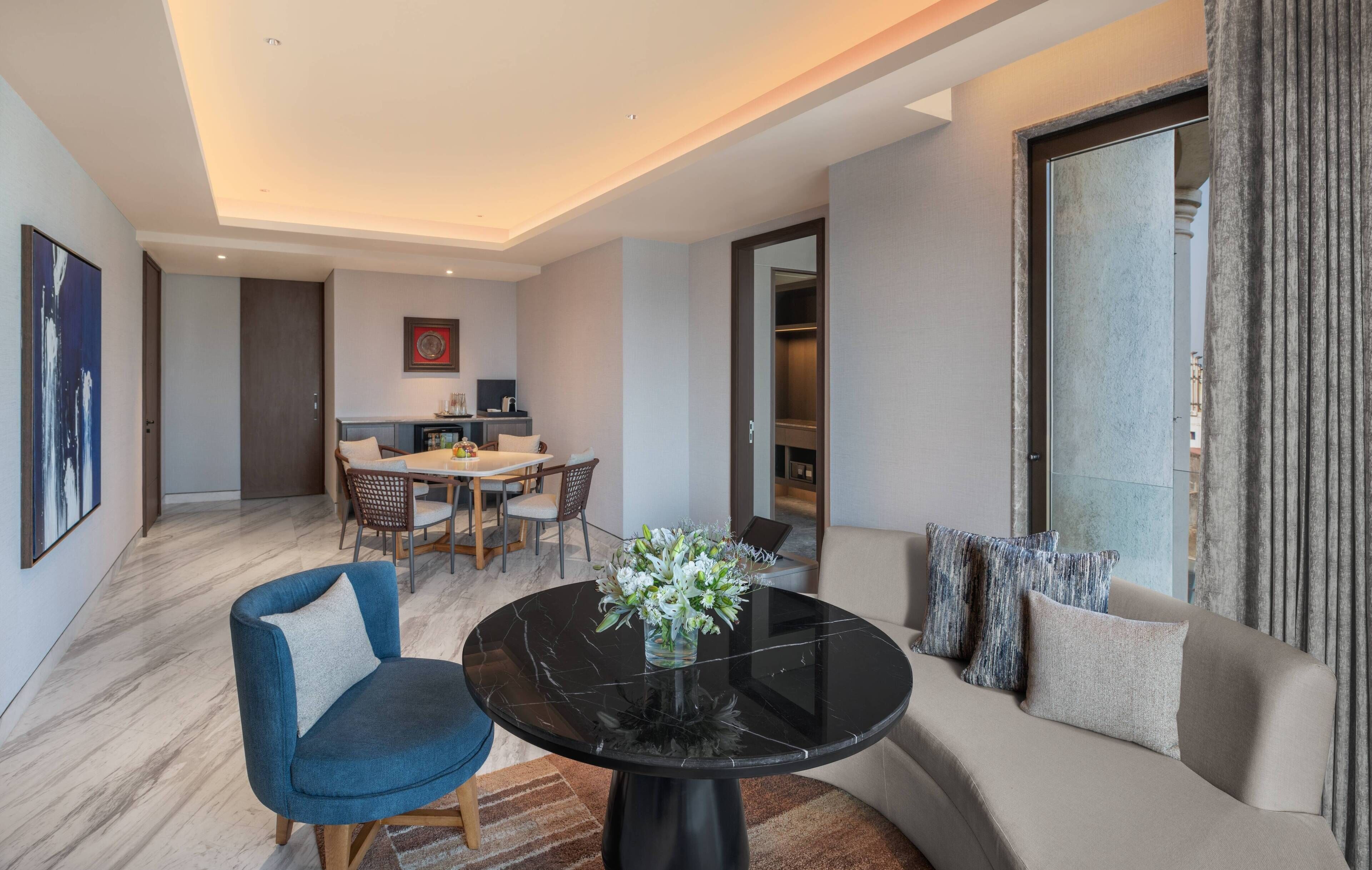A modern living room with a round black table, a sofa, and a dining area with chairs and a table.