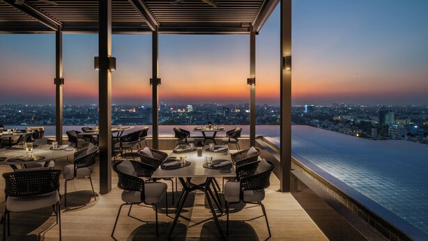 A rooftop restaurant with tables and chairs, overlooking a cityscape at sunset. - The Residency Towers (Chennai)
