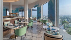 A modern restaurant with high ceilings, large windows, and a city view. - The Residency Towers (Chennai)