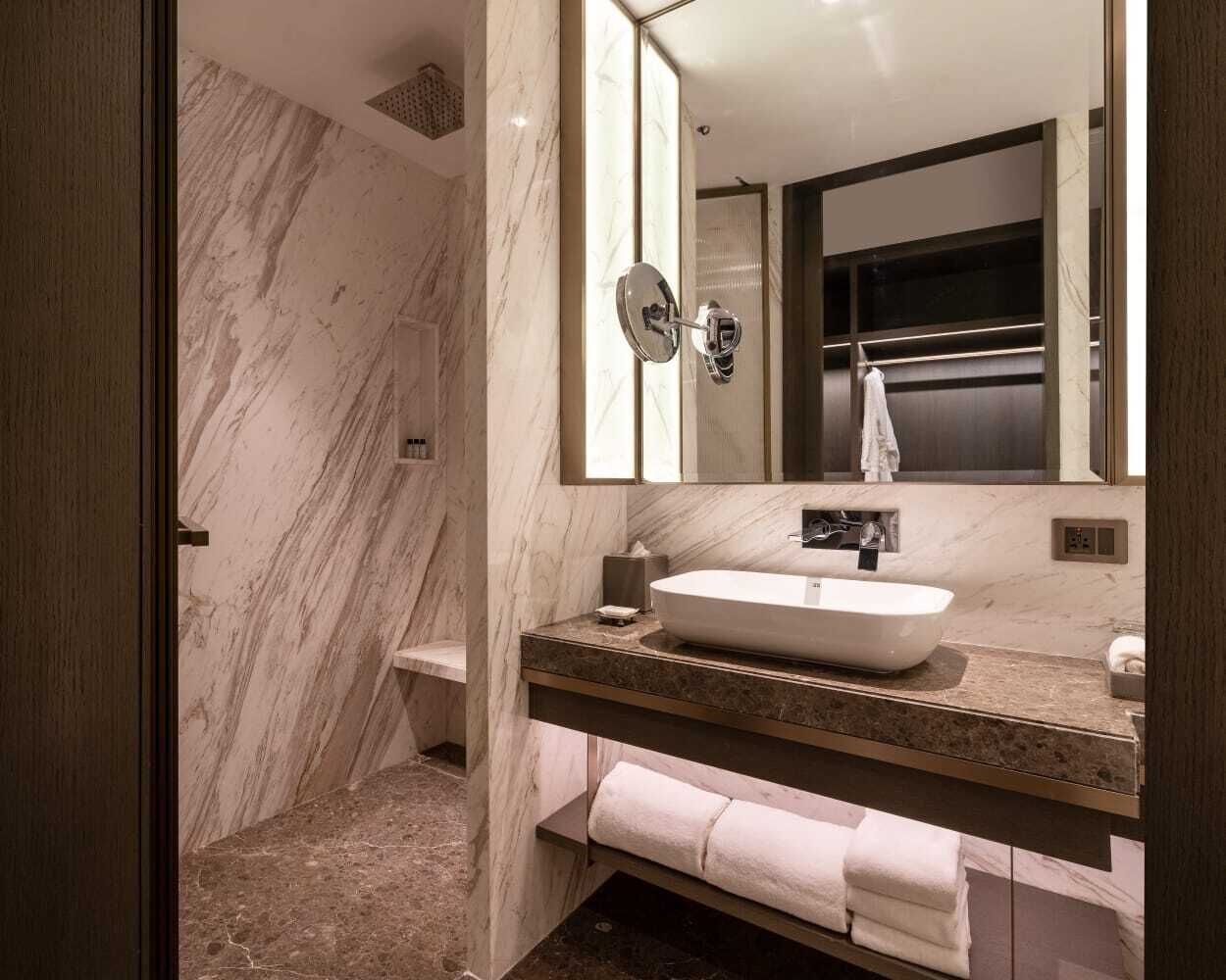 A modern bathroom with a marble wall, a large mirror, a sink, and a shower area.