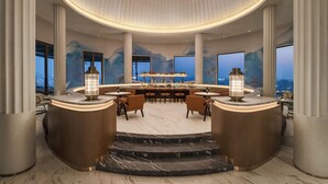 A luxurious bar area with a central bar, seating, and large windows offering a city view. - The Residency Towers (Chennai)