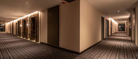 A hotel hallway with a checkered carpet, glass doors, and a red fire alarm.