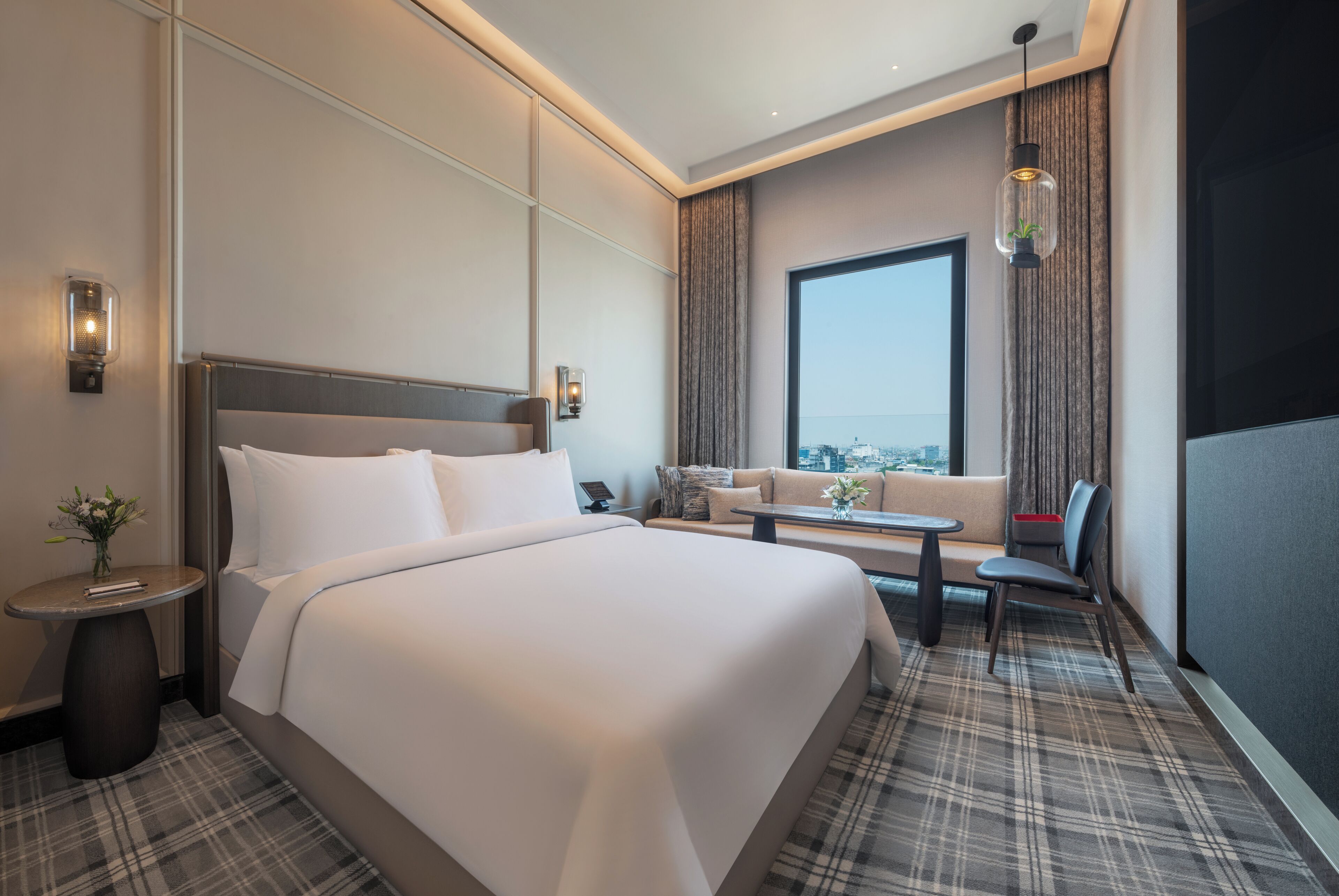 A modern hotel room with a large bed, a sofa, a small table, and a city view.