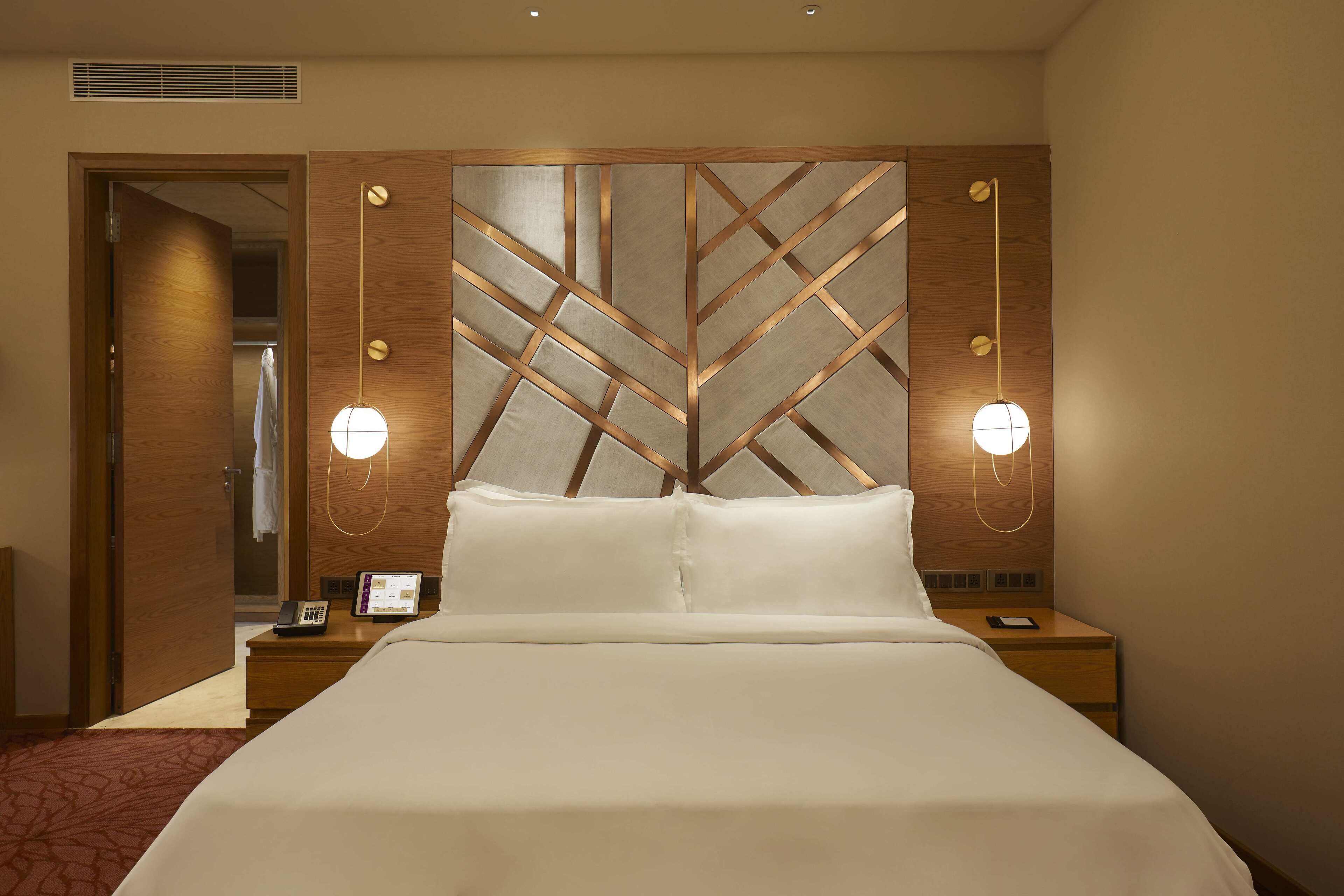 A hotel room with a large bed, bedside tables, a phone, and wall-mounted lights.