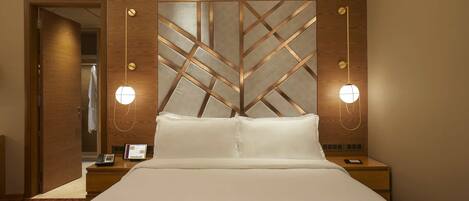 A hotel room with a large bed, bedside tables, a phone, and wall-mounted lights.