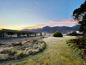 A motel with a simple, single-story structure, a covered parking area, and a view of mountains in the distance. - Glacier View Motel (Franz Josef Glacier)