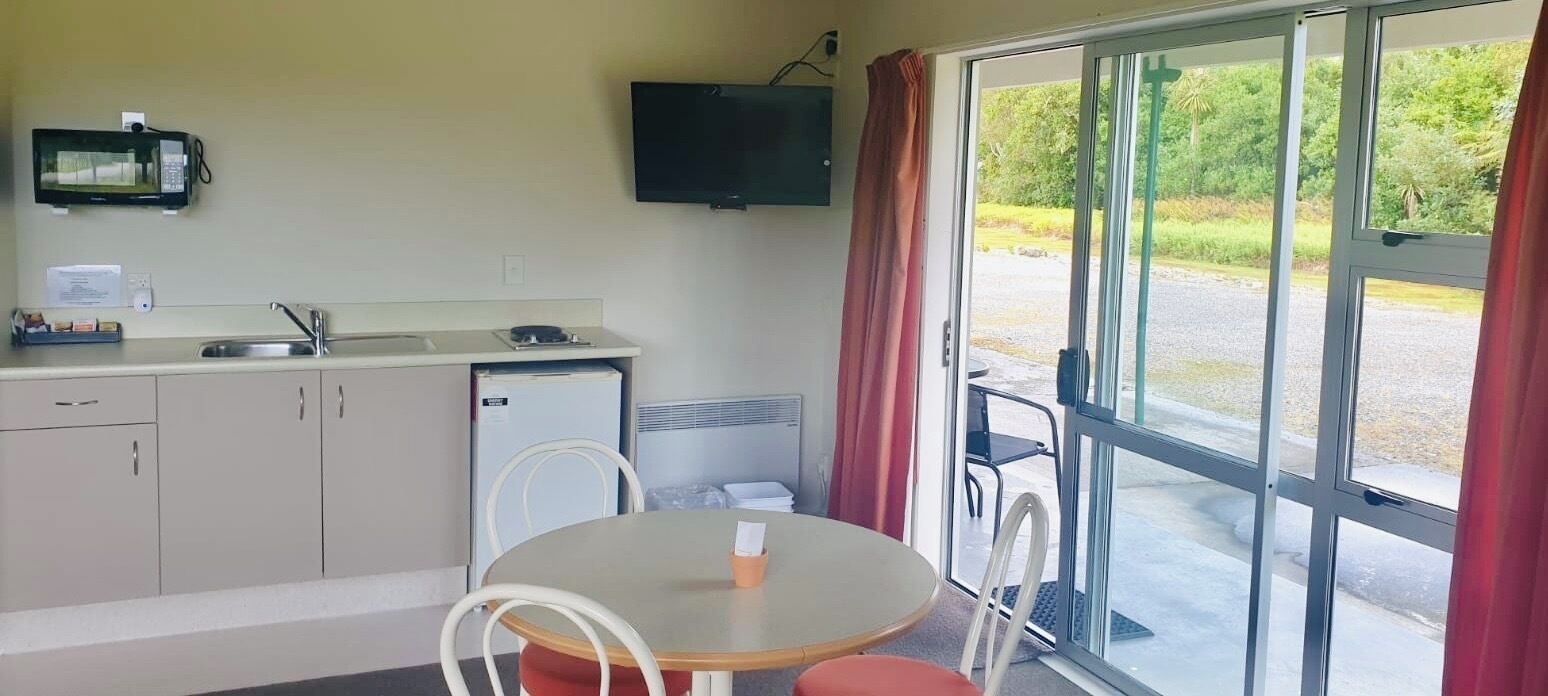 A compact kitchenette with a microwave, sink, and small refrigerator. There is a dining area with a table and chairs, and a large sliding glass door leading to an outdoor area.