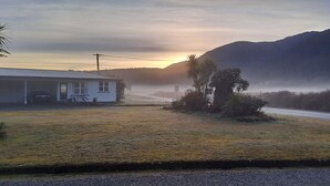 Uma casa com garagem, entrada de veículos e estrada que leva a uma montanha.