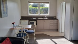 Uma cozinha compacta com janela, uma área de jantar com mesa e cadeiras, e uma porta que dá para outro cômodo.