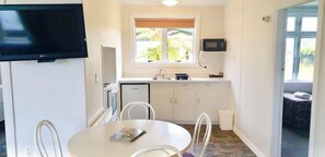 A compact kitchen with a microwave, a sink, and cabinets. There is a dining area with a table and chairs, and a television mounted on the wall. - Glacier View Motel (Franz Josef Glacier)