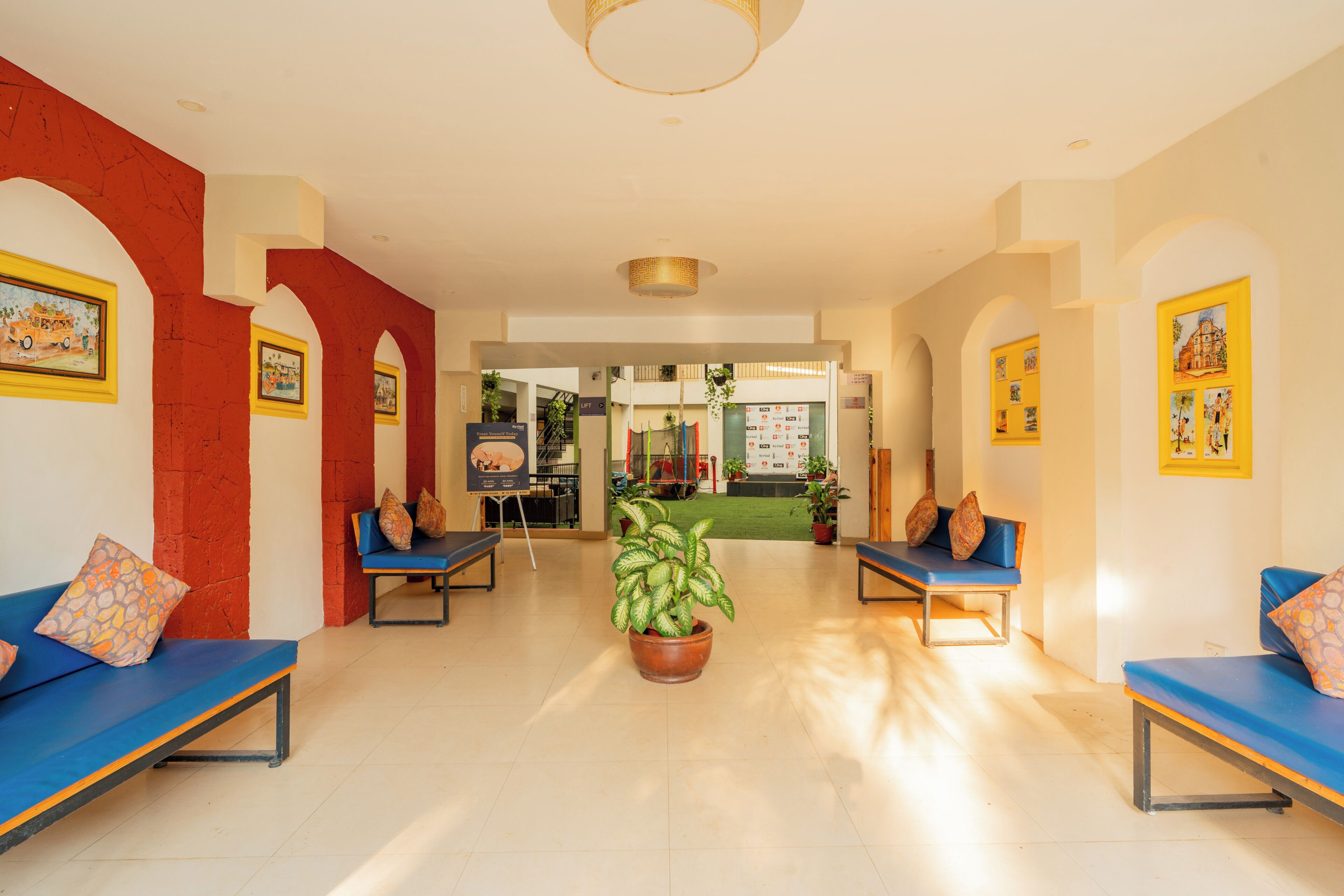 A hotel lobby with blue seating, a central potted plant, and framed artwork on the walls.
