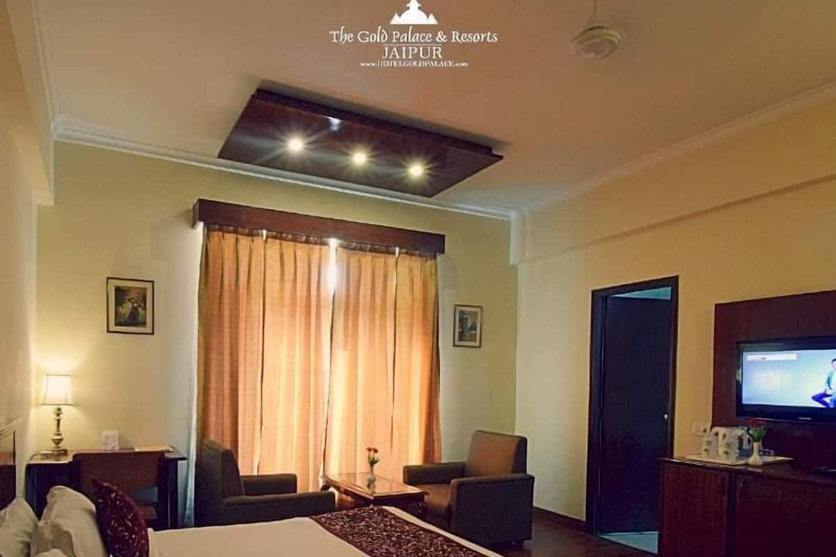 Habitación de hotel con cama, dos sillas, televisión y escritorio con lámpara.