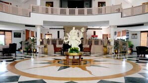 Un vestíbulo amplio con una estatua central, techos altos y un patrón de piso a cuadros.