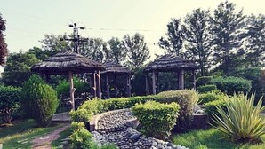 Un jardín con gazebos de techo de paja, un sendero de piedra y abundante vegetación.