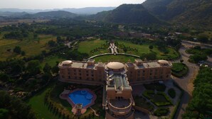 Un hotel grande de varios pisos con un patio central, rodeado de abundante vegetación y montañas al fondo.